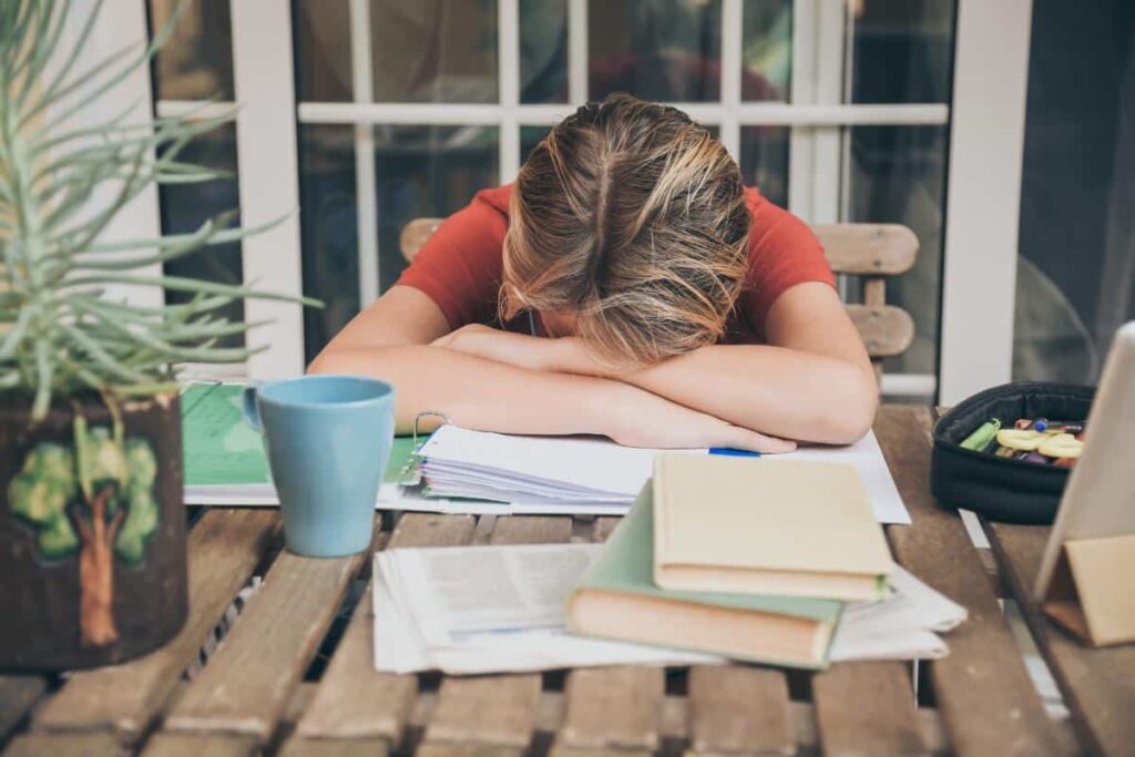a young person rests on some books at a table struggling with adhd in teens