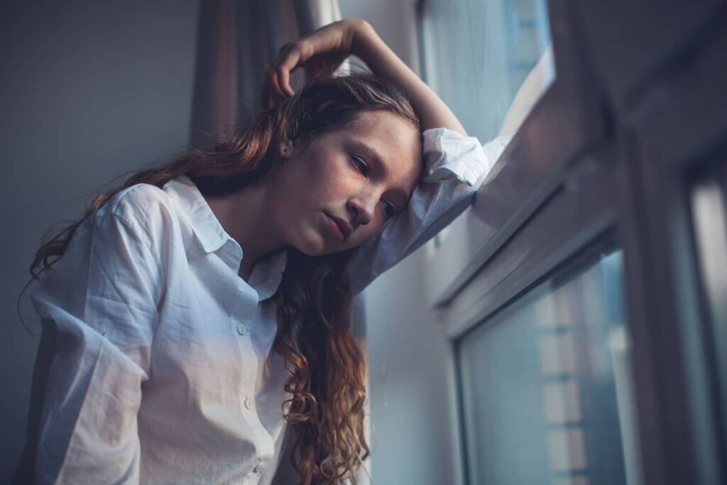 a teen looks sadly out of a window battling a depression crisis