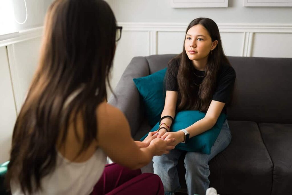a teen holds hands with a therapist after discussing medication management for addiction