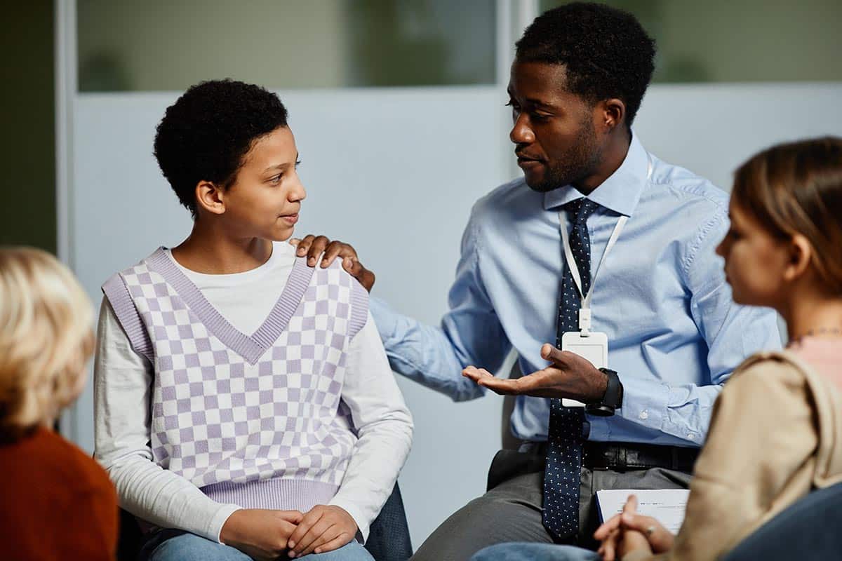 a counselor puts their hand on a person's shoulder in Teen Group Therapy